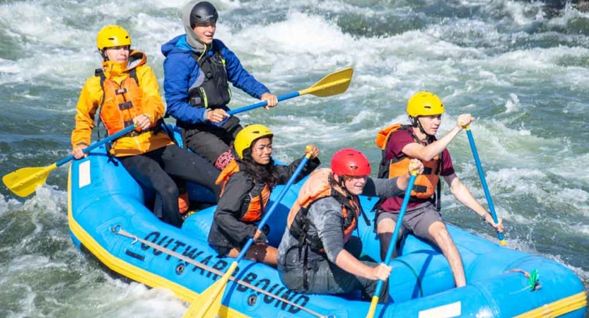 a group of gap year students use paddles to navigate whitewater on an outward bound course